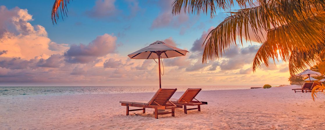 Tranquil sunset on the beach with reclining chairs and a parasol, wide