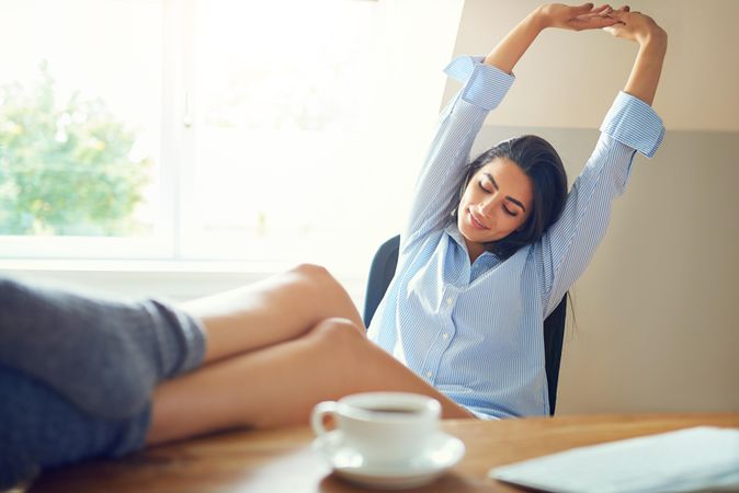 Woman at her office desk stretching her arms up with feet on desk