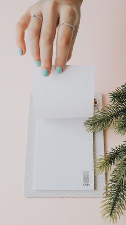 Person opening empty page of clipboard notes on table with fir branch