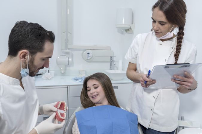 Male dentist showing dental jaw model to female patient in dentist's office