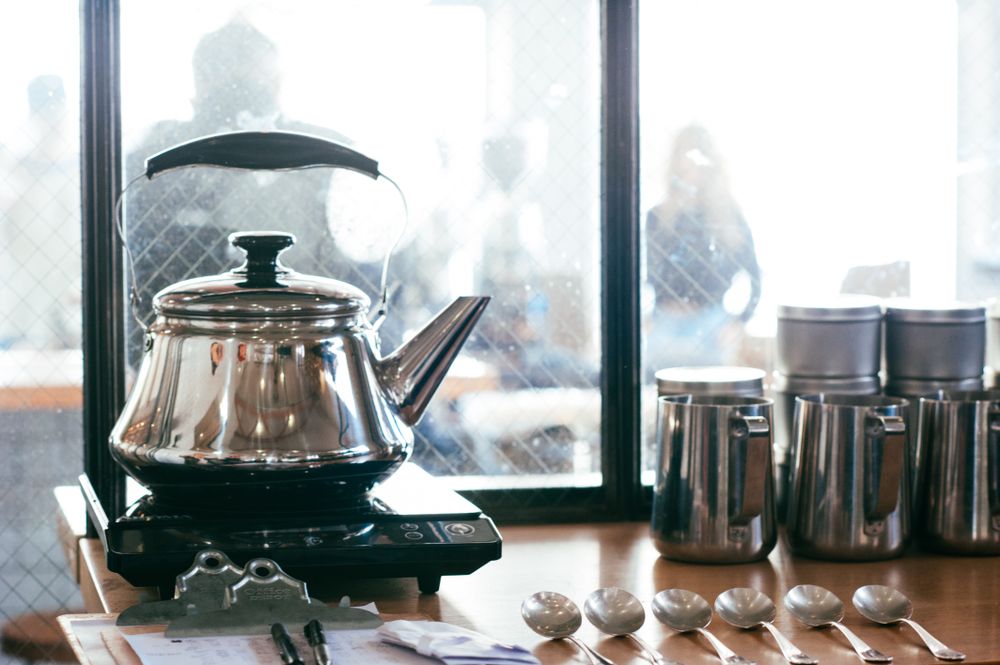 Silver kettle heating up water for coffee tasting with coffee shop in background