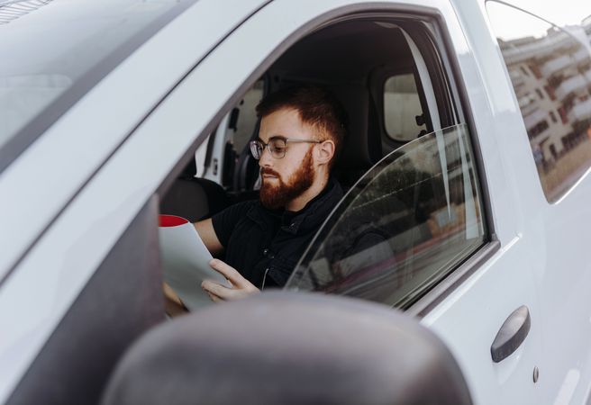 Courier filling papers while preparing for delivery of order to client in car