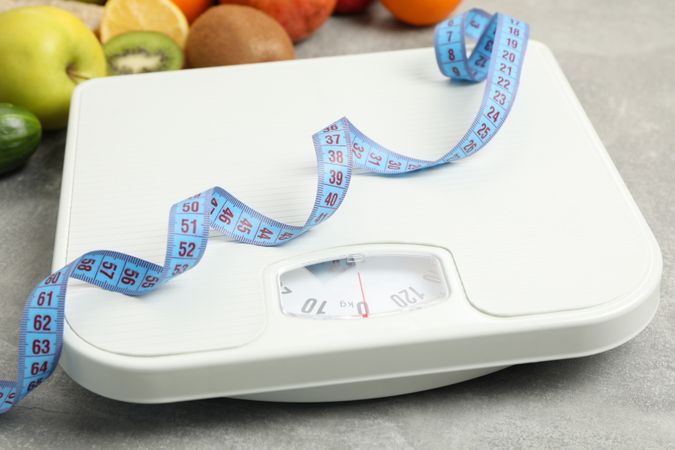 Scales, measuring tape and vegetarian food on gray background