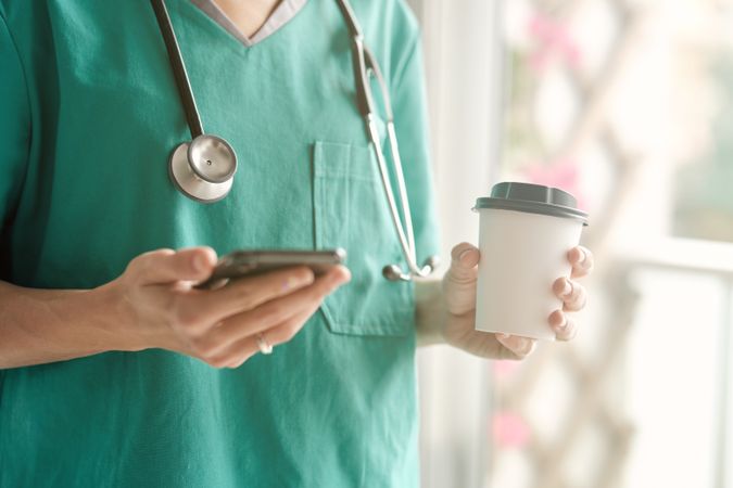 Crop surgeon with smartphone and coffee to go during break