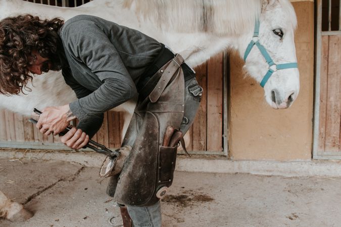 Man shoeing horse near stable