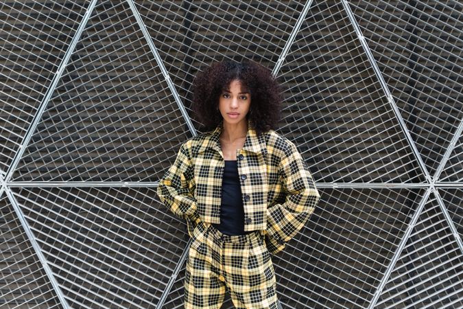 Stylish woman with Afro hairstyle against grid fence