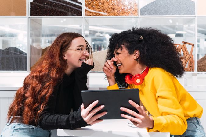 Positive multiethnic female friends using tablet and laughing in cafe