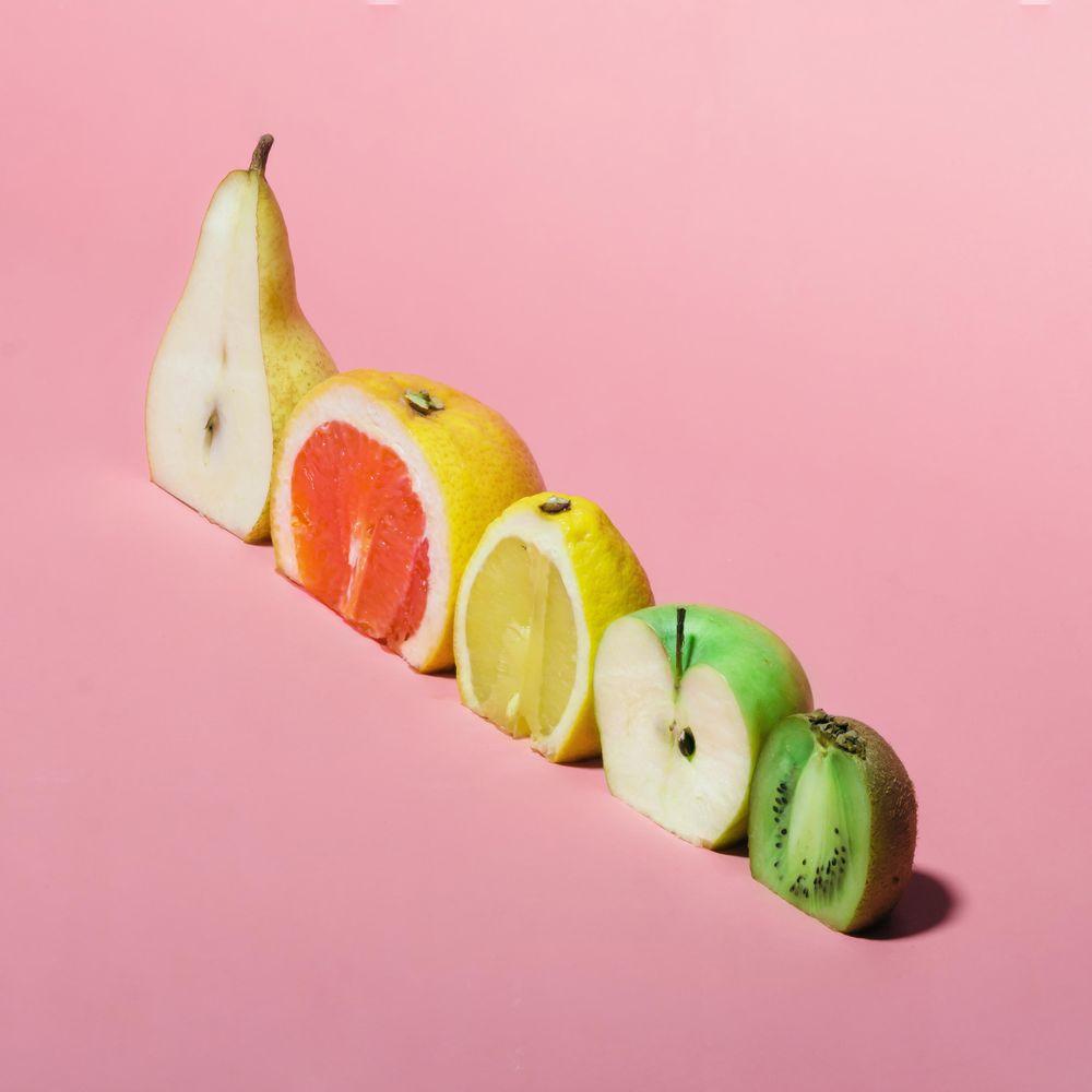 Various fruits sliced in half showing cross-section on pastel pink background