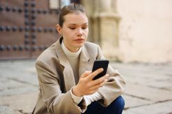 A Young Woman is Engaged with Her Smartphone While Sitting Outdoors in a Public Space