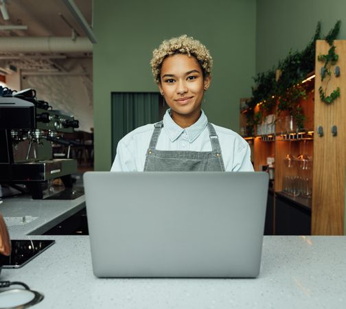 Content female working in cafe with laptop behind counter