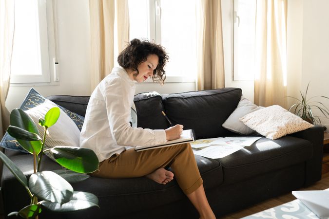 Woman writing on paper on sofa in room