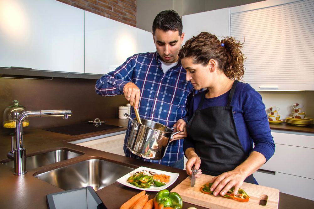 Woman cutting vegetables while her husband stands next to her with the pot
