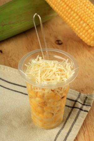 Cup of Indonesian sweet corn dessert with condensed milk and grated cheese served with plastic spoon