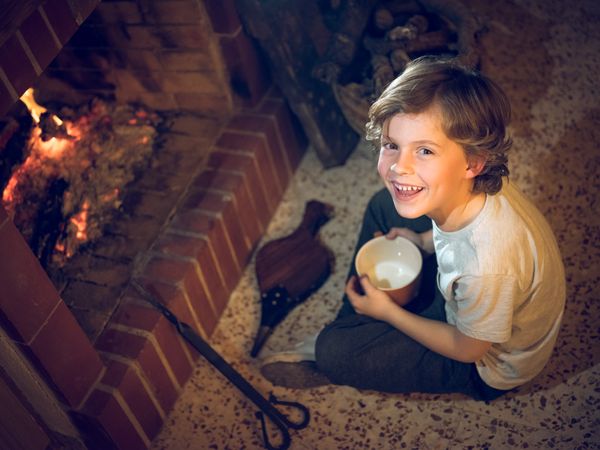 Little boy sitting on floor opposite burning fireplace