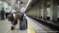 Two children with light hast and backpacks waiting at train station in Japan 4OqMa0