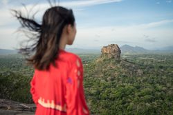 Tourist against solitary rock in middle of green forested plain under clear sky in summer