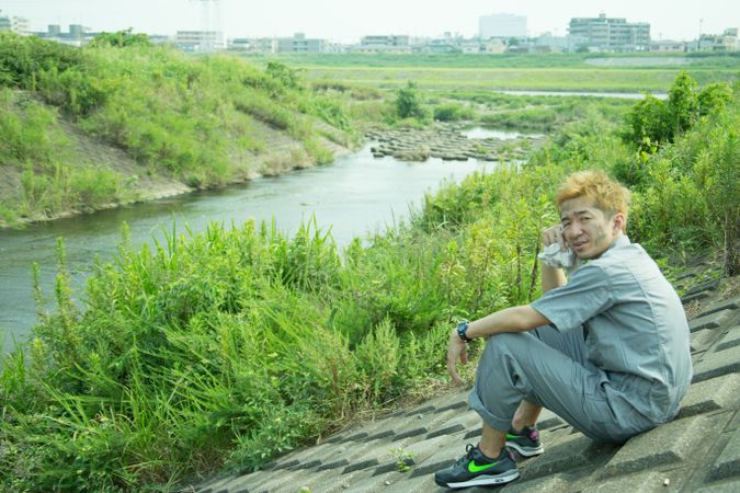 Drained man sitting on concrete ground near river stream