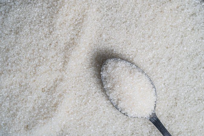 Granulated sugar spread on a surface with a spoonful resting on top