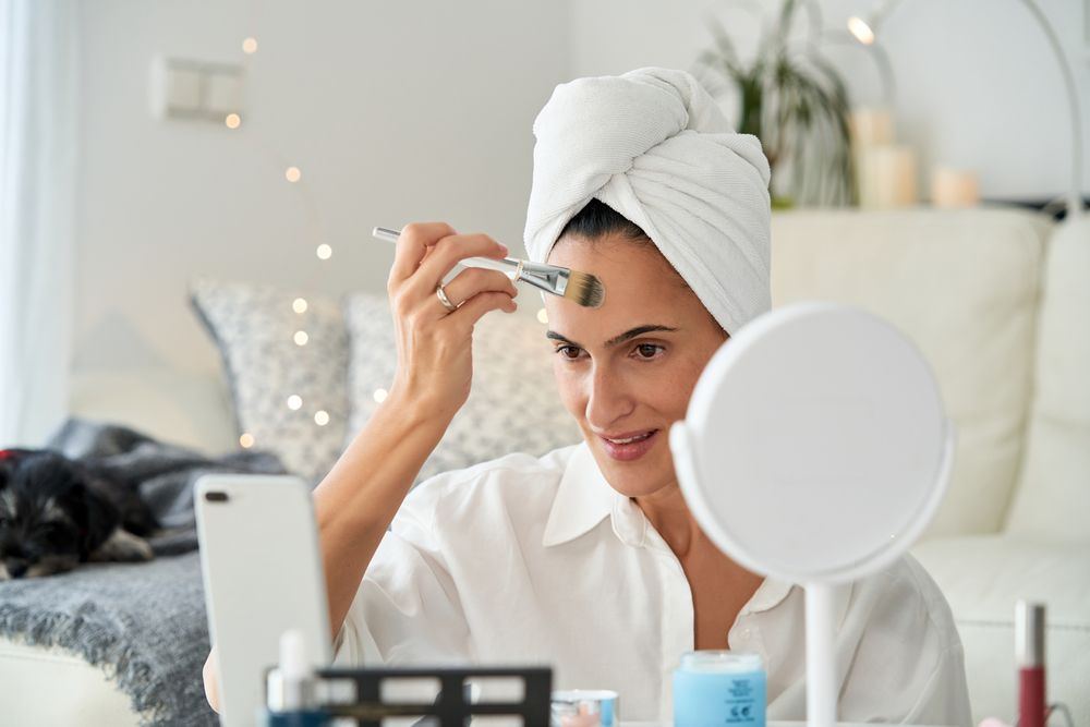 Smiling woman with smartphone applying makeup