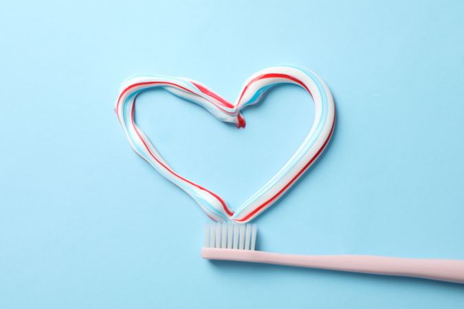 Heart made of toothpaste and toothbrush on blue background, top view