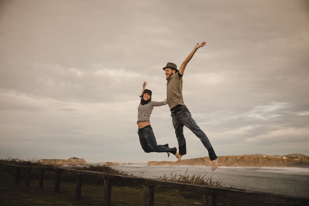 Couple holding hands and jumping on bench on shore near water