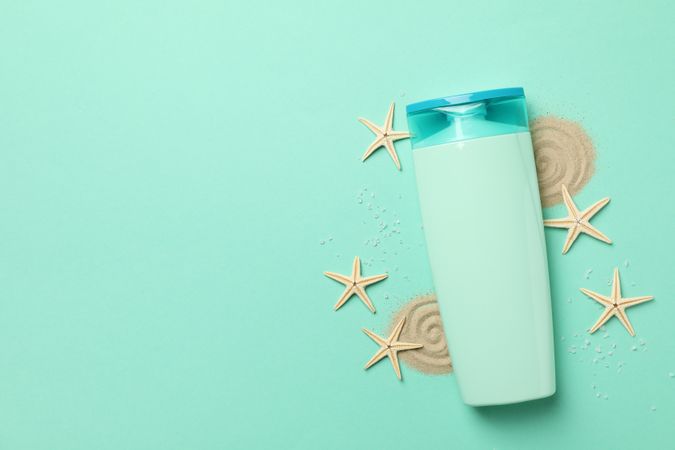 Bottle of shampoo, starfishes and sand on mint background
