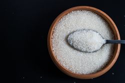 Flat lay of a wooden bowl filled with sugar and a stainless spoon resting on top