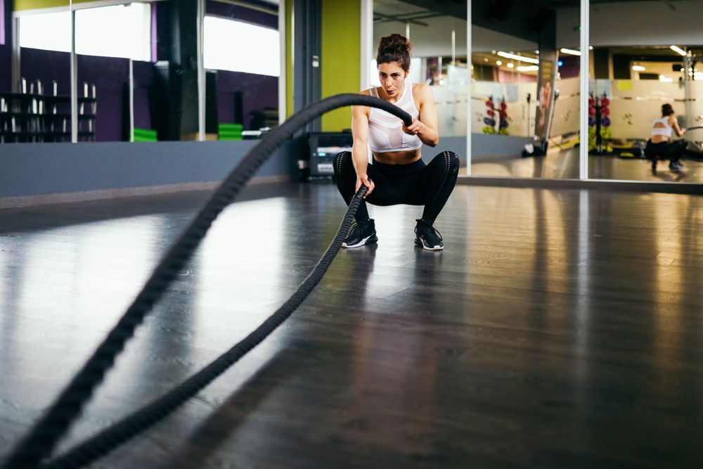 Woman working out upper body with ropes in gym and squatting