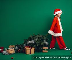 Girl dressed as Santa Claus walking holding a Christmas tree 5loam0