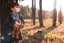 Young boy holding teddy bear and both wearing masks