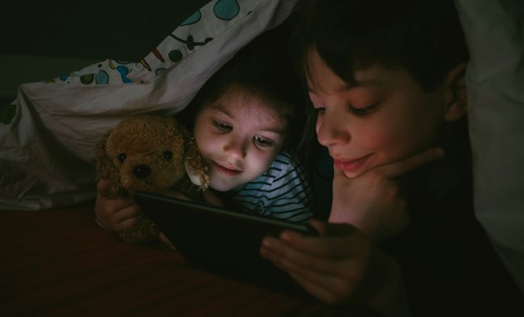 Siblings looking at the tablet in the dark