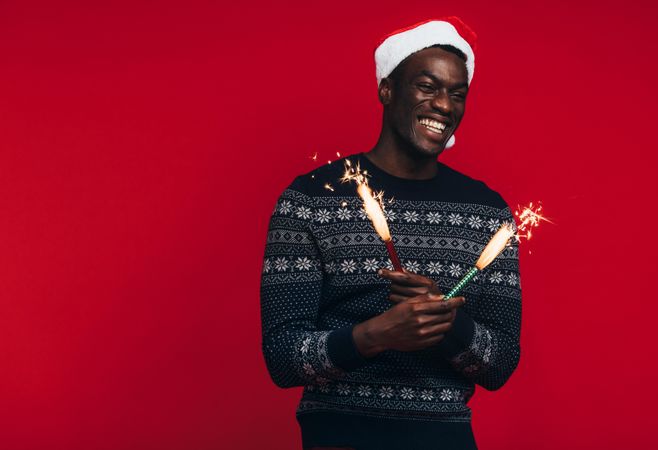 Cheerful young Black man in Santa hat celebrating with sparklers