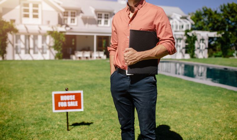 Man holding folder of documents outside an affluent house for sale
