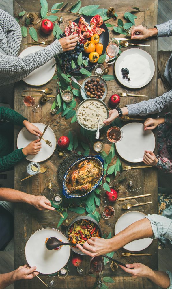 Group serving themselves at festive table with roasted chicken, pomegranates, vertical composition
