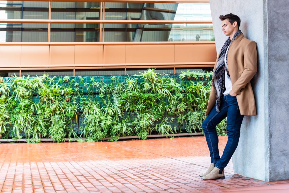Serious man in camel coat looking away leaning on wall outside