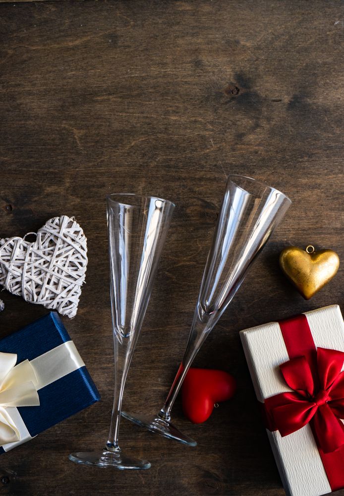 Top view of two glass champagne flutes with gifts and heart ornaments with copy space