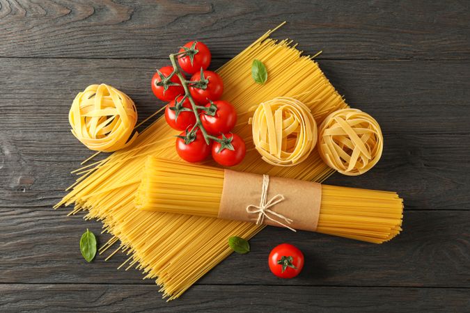 Composition with pasta, tomatoes and basil on wooden background, space for text and top view
