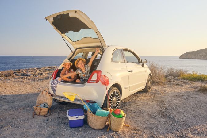Two children sitting inside the trunk of the car with gestures o