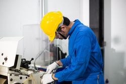 Male in blue jumpsuit and PPE gear operating machinery in factory