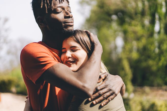 Multi-racial couple with Black man and white woman embracing each other intimate outdoors in the park