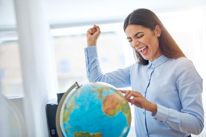 Woman with finger on globe with one fist up in celebration
