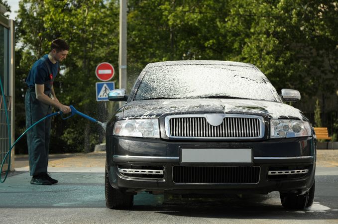 A man washes a car in a manual car wash. Clear car