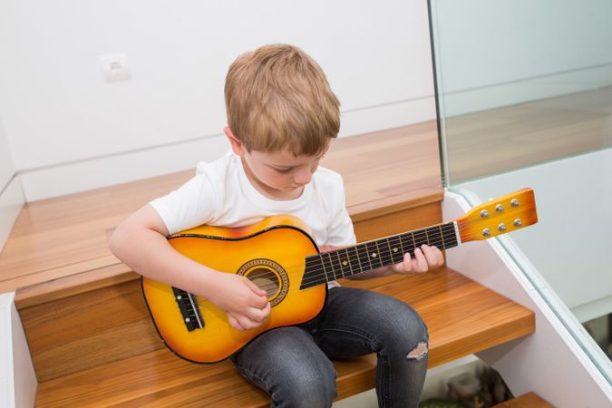Young blonde boy playing toy guitar