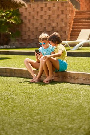 Cheerful boys browsing smartphone sitting on garden