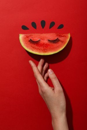 A slice of watermelon with decorative eyelashes on a red background