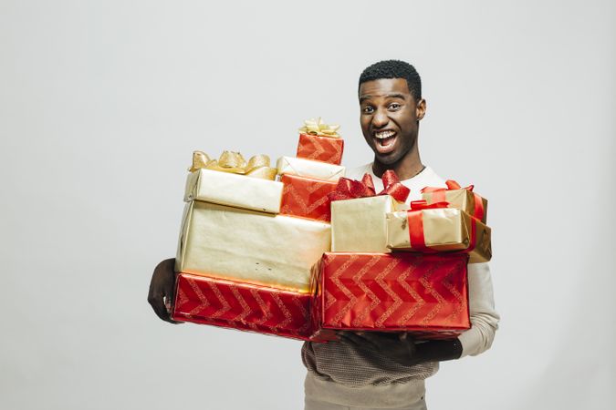 Excited Black man holding pile of wrapped presents in both arms