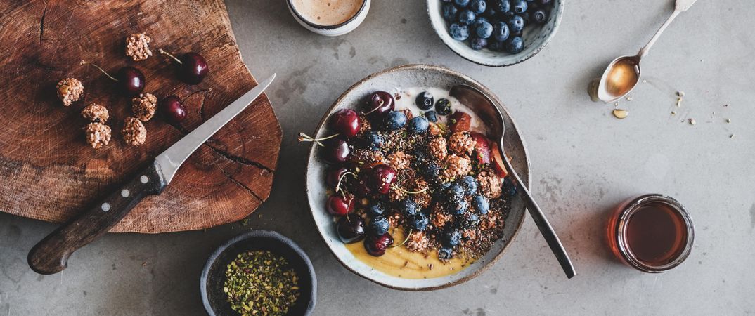 Oat granola yogurt bowl with cherries, blueberries, honey, nuts, coffee, wooden board