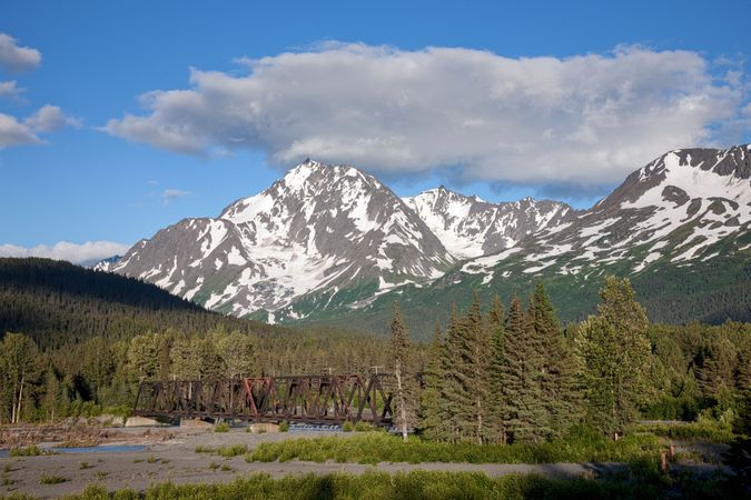 Majestic snowy peaks with trees and rusty bridge in Chugach, Alaska