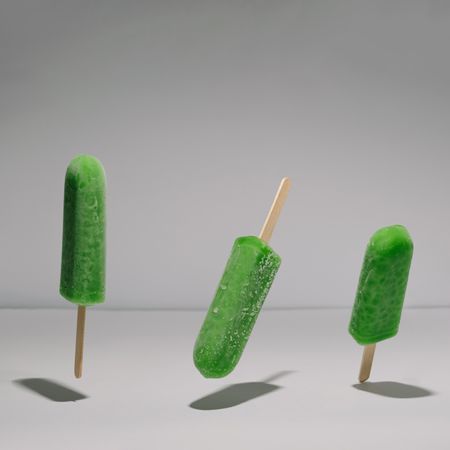Three green ice pops suspended with shadow in grey room