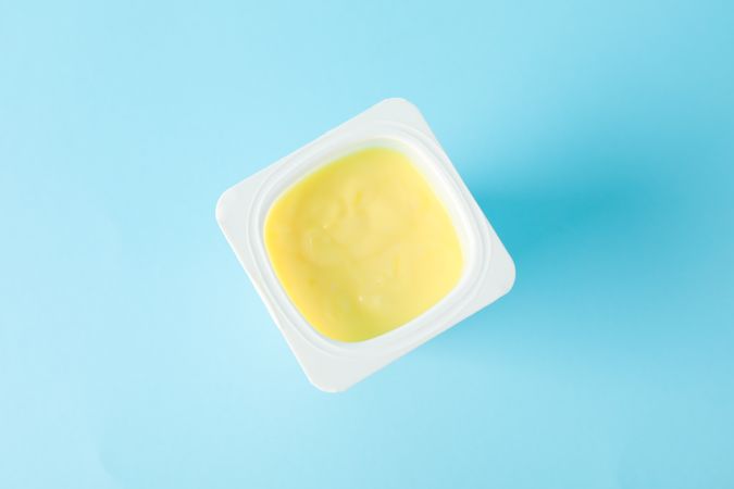 Plastic cup with yogurt on color background, space for text
